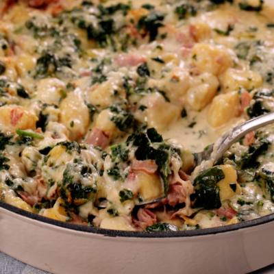 a fork scooping up Cheesy Spinach and Ham gnocchi in a skillet