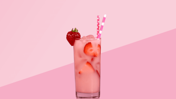 Clear glass filled with a pink drink and strawberries in front of a pink background