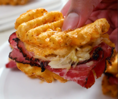 Hand holding a waffle fry Reuben slider