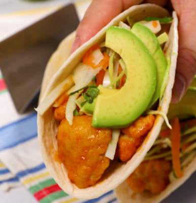 A hand holding a taco with avocado and chicken inside